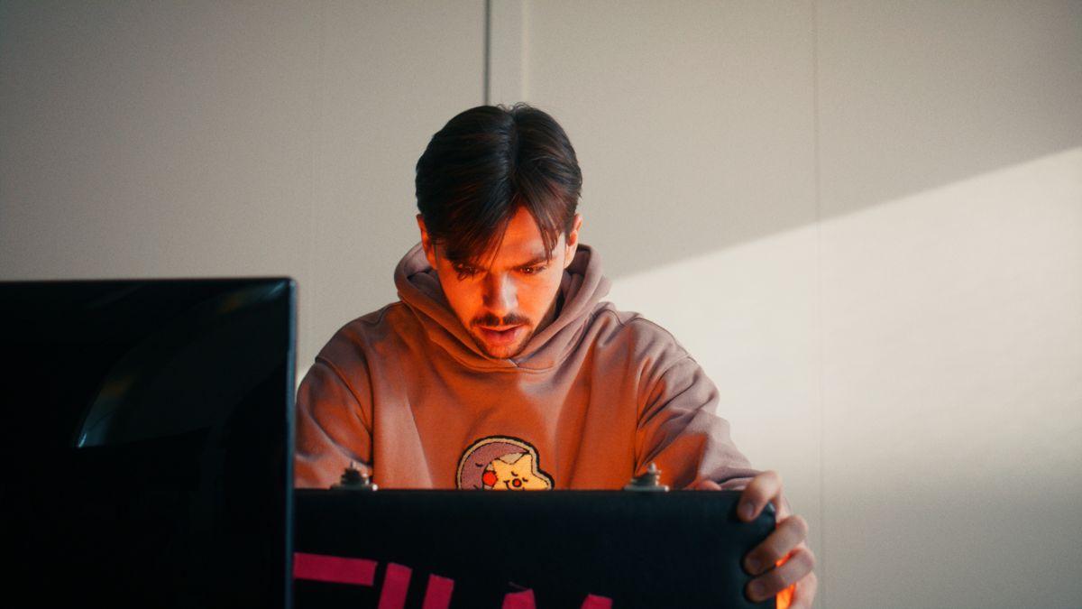 Een man in een oranje hoodie klapt een laptop dicht. Still uit een MediaTuig-commercial, 2024.